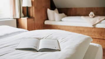 Ein ordentlich bezogenes Bett mit offenem Buch, einer Lampe auf dem Nachttisch und einem Holz-Kopfstück.