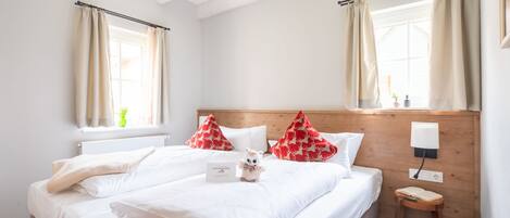 A neatly made bed with white linens, a small bedside table with a lamp, and red and white patterned pillows.