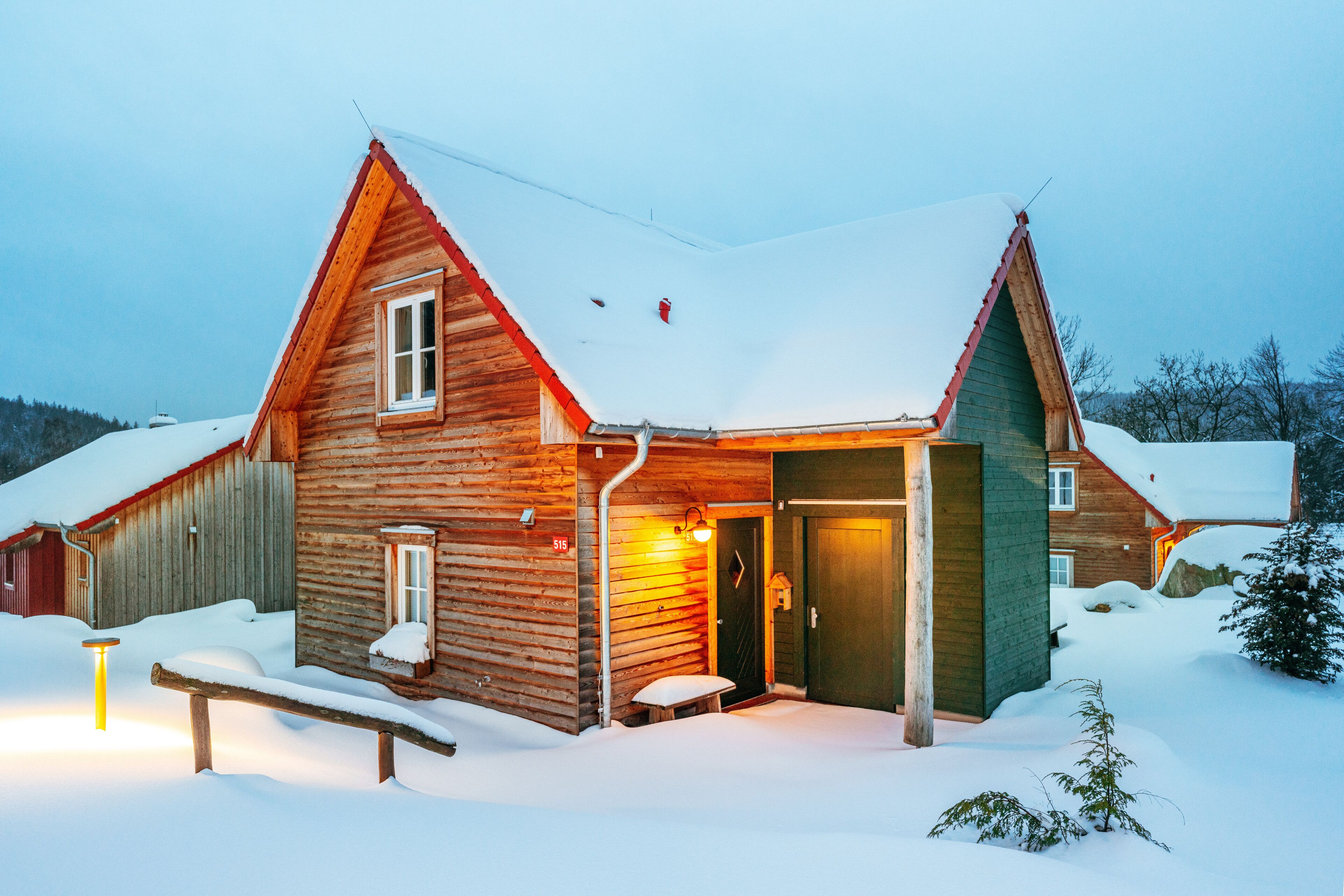 A wooden cabin with a snow-covered roof and a bench outside.