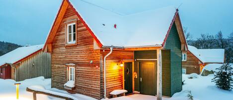 A wooden cabin with a snow-covered roof and a bench outside.