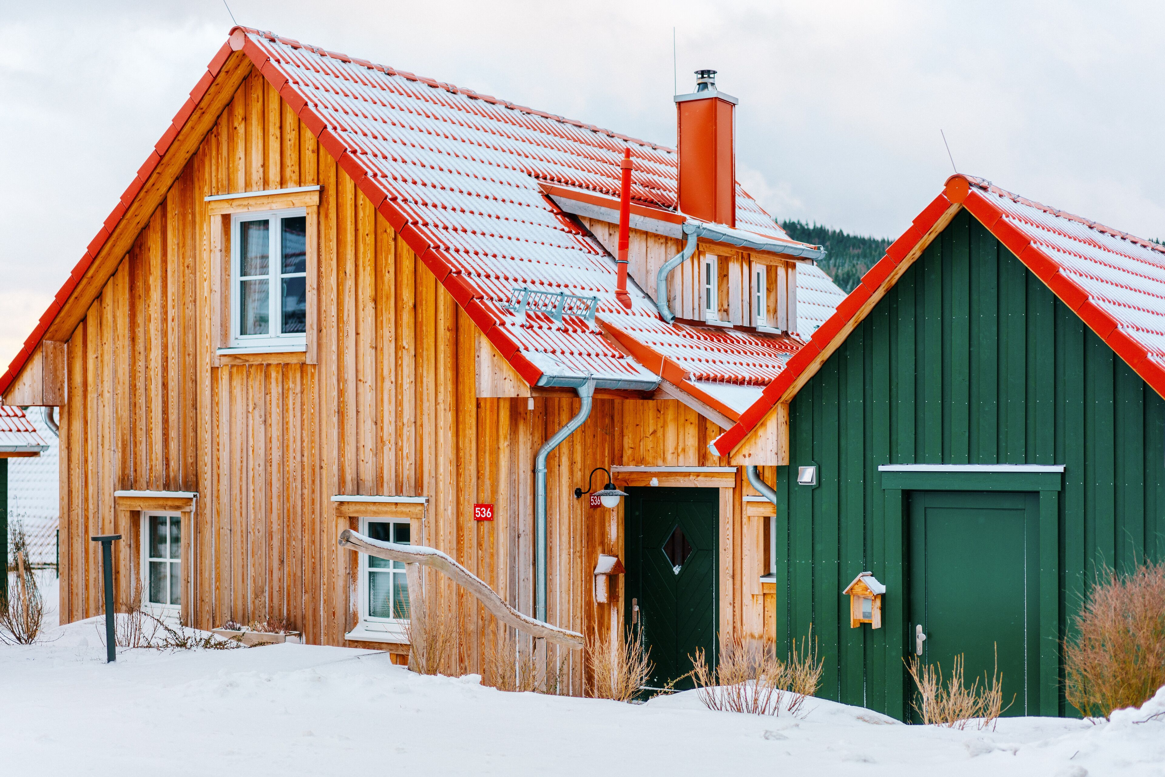 Una cabaña de madera con techo rojo y puerta verde, rodeada de nieve.