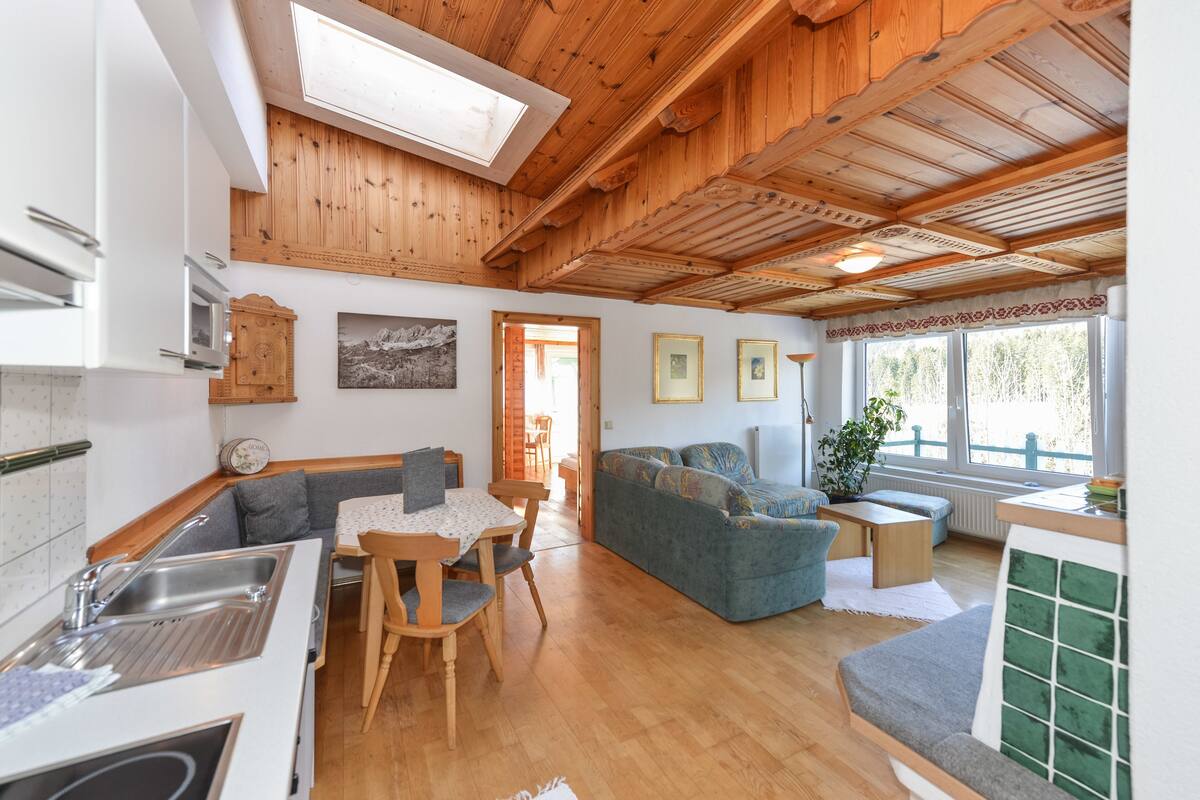 Een gezellig interieur met een houten plafond, een eethoek met een tafel en stoelen, een bank en een keuken met een spoelbak en kastjes.
