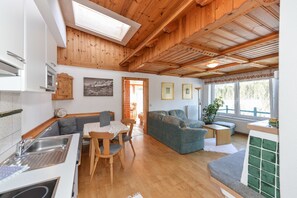 A cozy interior with a wooden ceiling, a dining area with a table and chairs, a sofa, and a kitchen with a sink and cabinets.