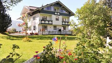 A two-story building with a balcony, surrounded by a well-maintained garden and a white picket fence.
