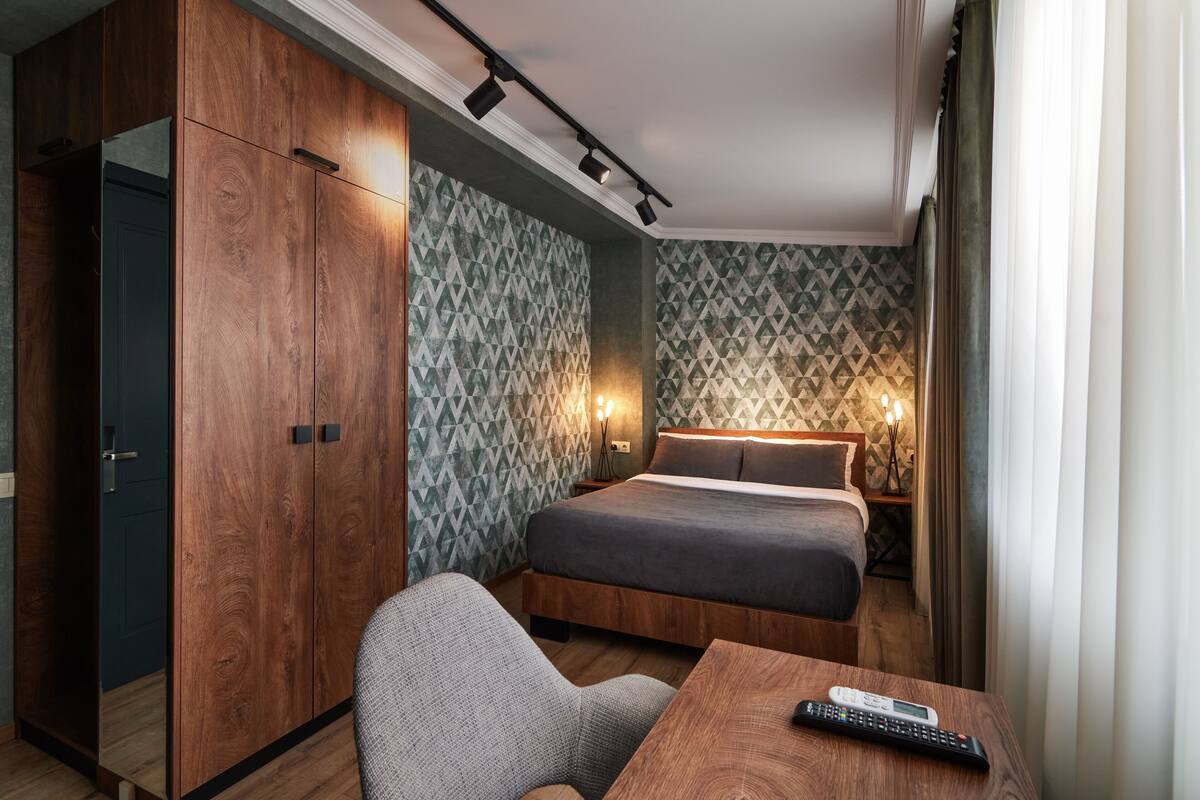 A hotel room with a bed, a desk, a chair, and a wardrobe.