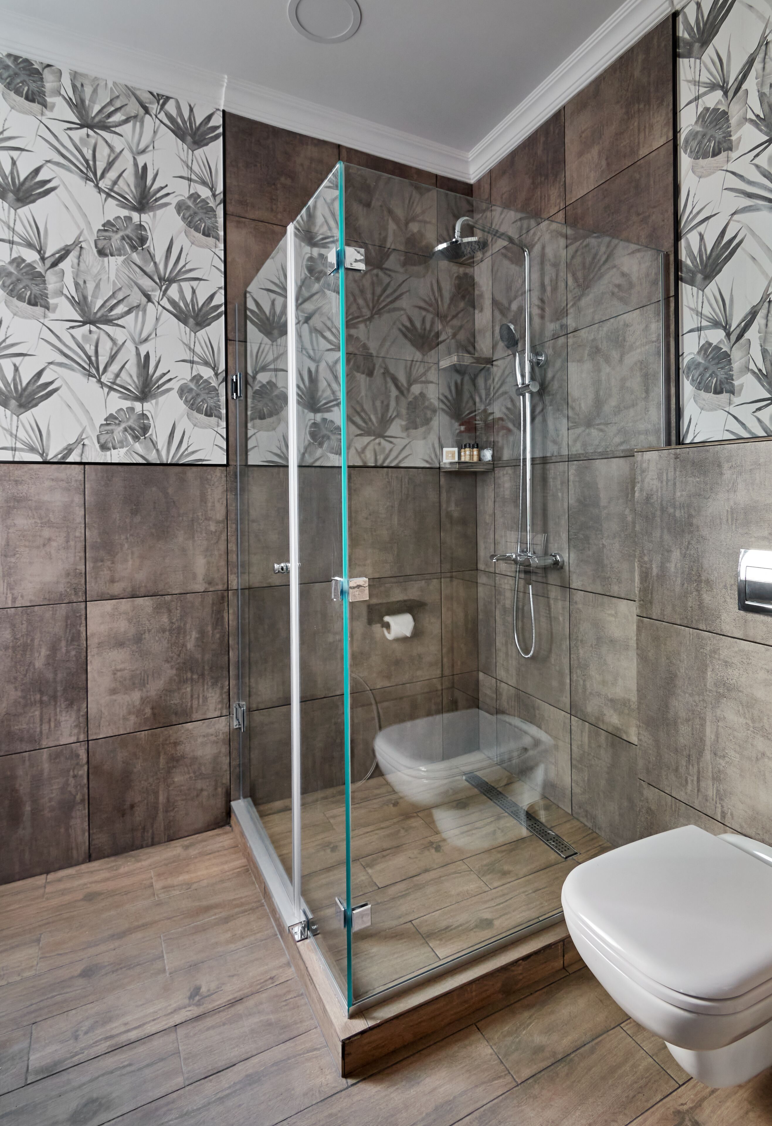 A modern bathroom with a glass-enclosed shower, a toilet, and a wooden floor.