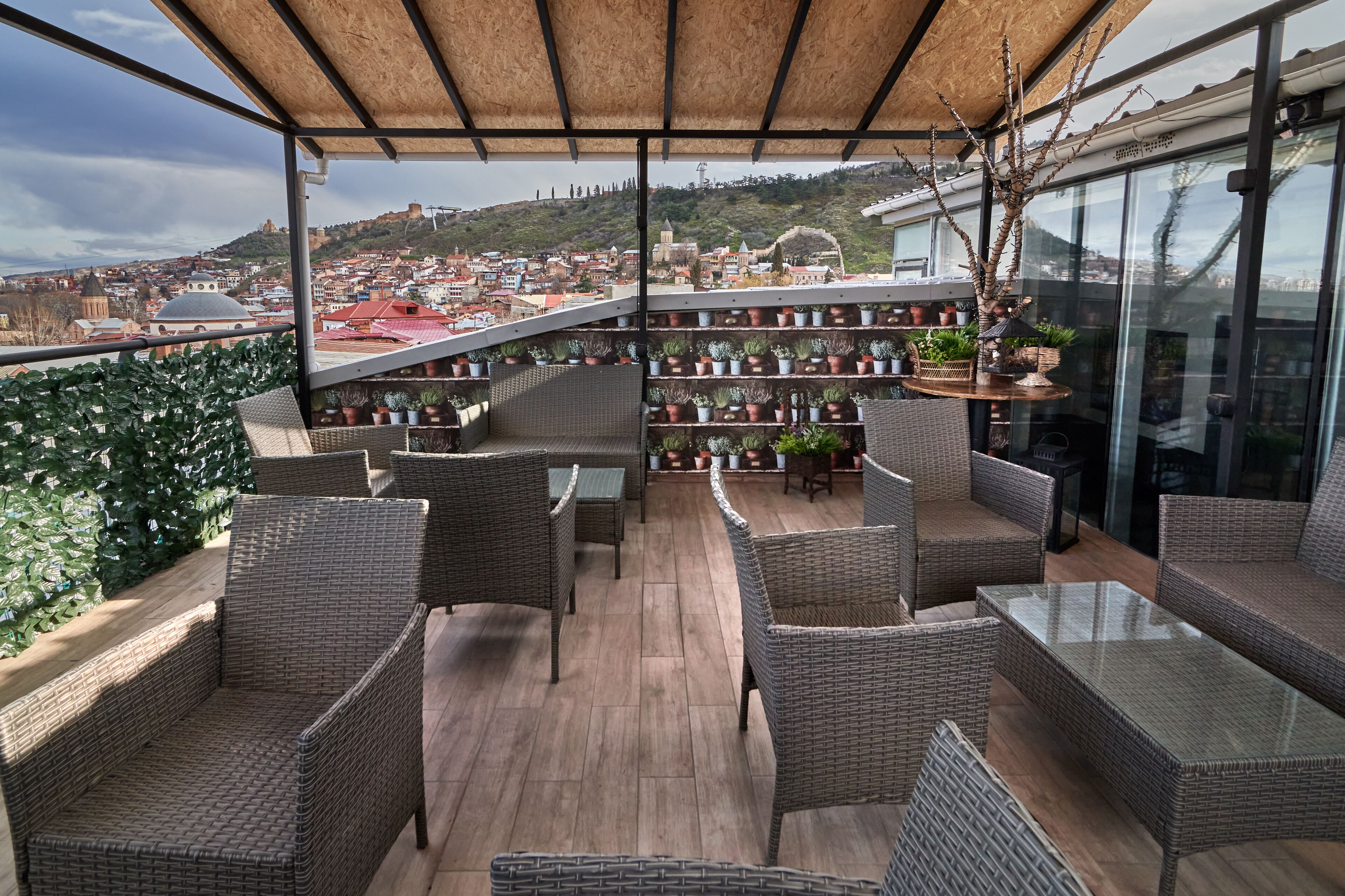A balcony with wicker furniture, potted plants, and a view of a cityscape.