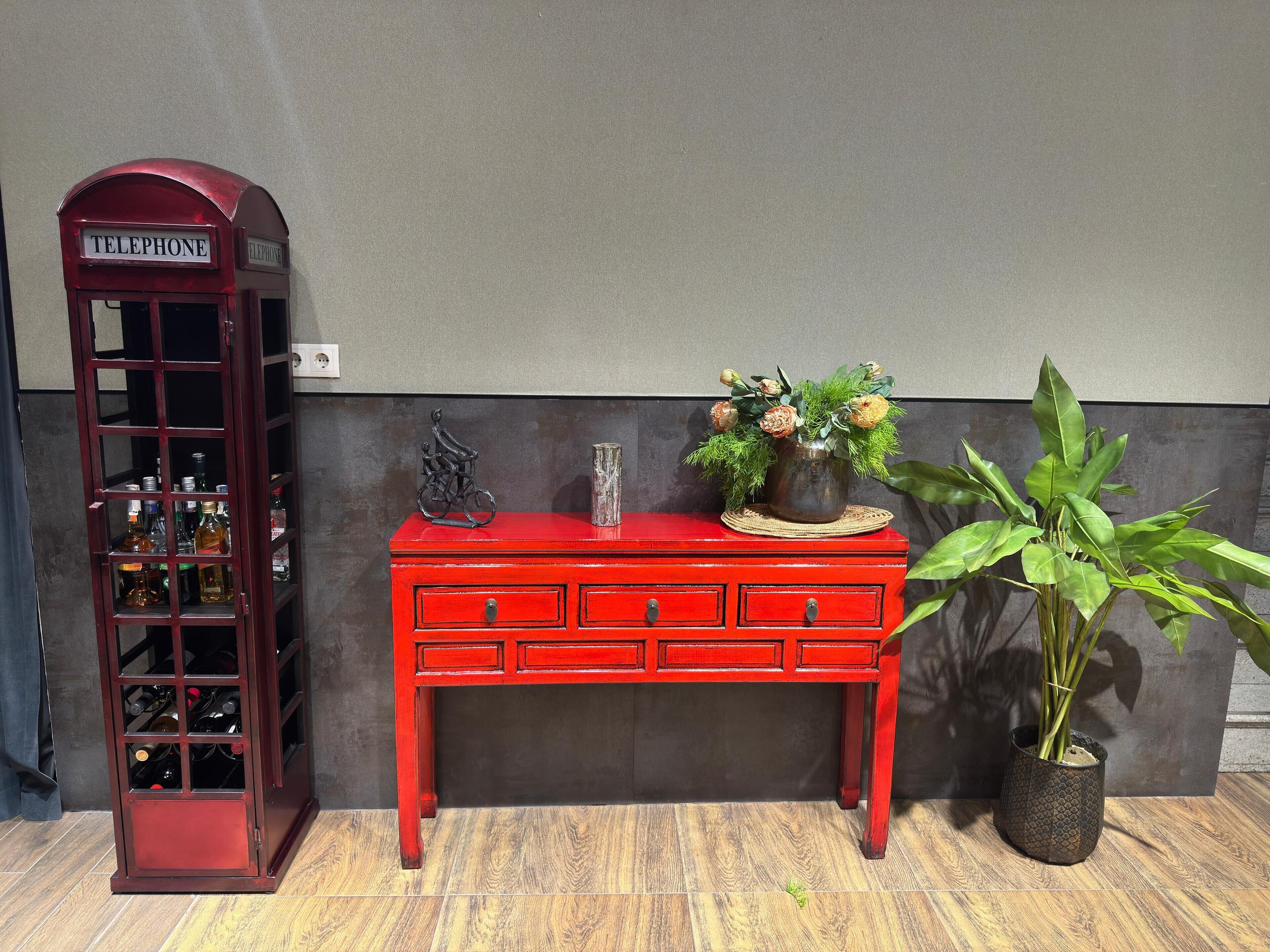 A red telephone booth, a red wooden cabinet with drawers, and a potted plant.