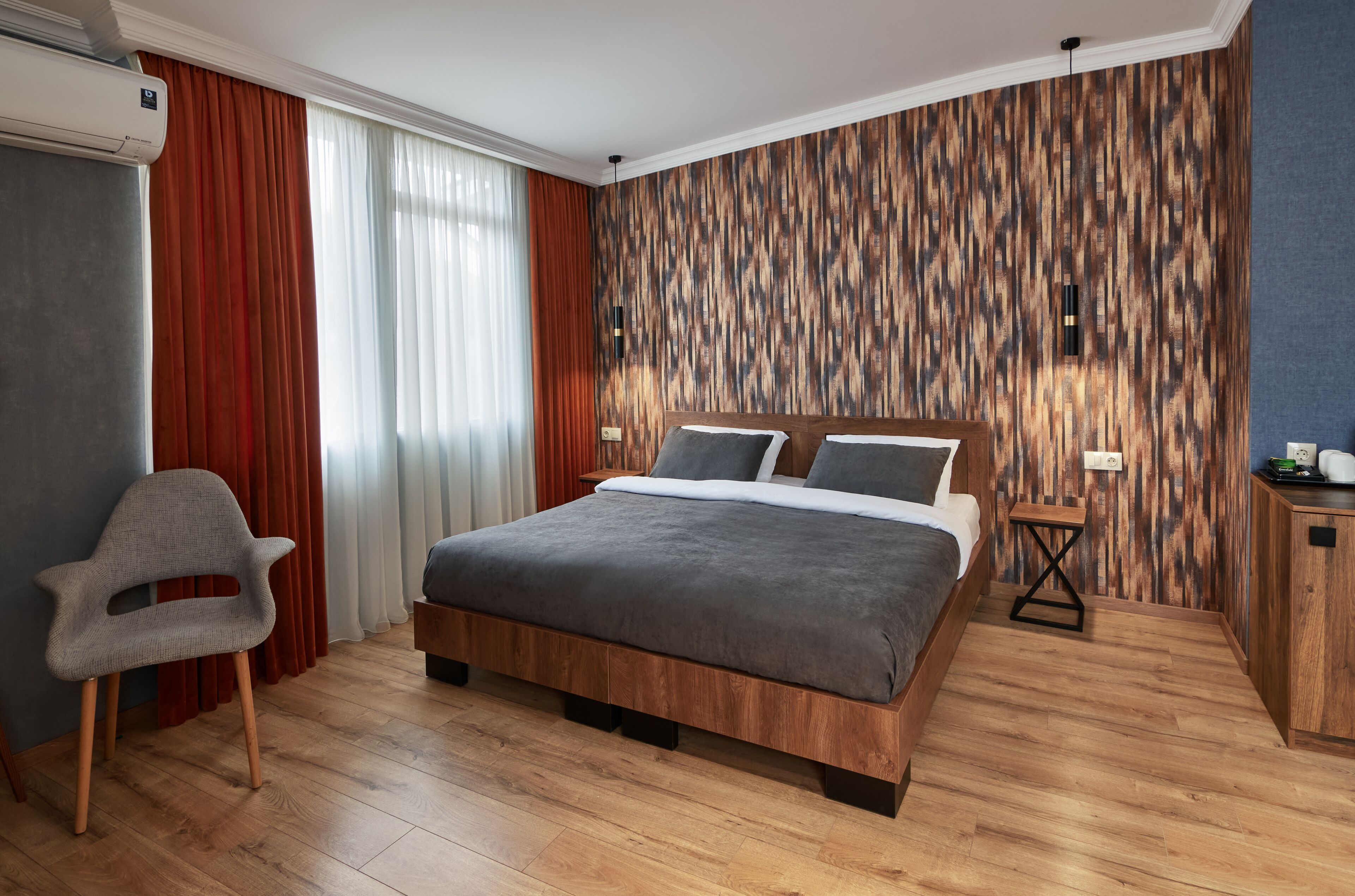A modern bedroom with a wooden bed, a grey chair, and a wooden wall panel.