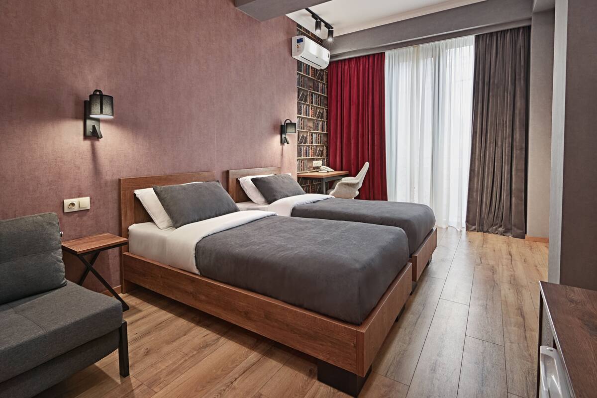 A modern hotel room with a wooden bed, a desk, a chair, and a bookshelf.