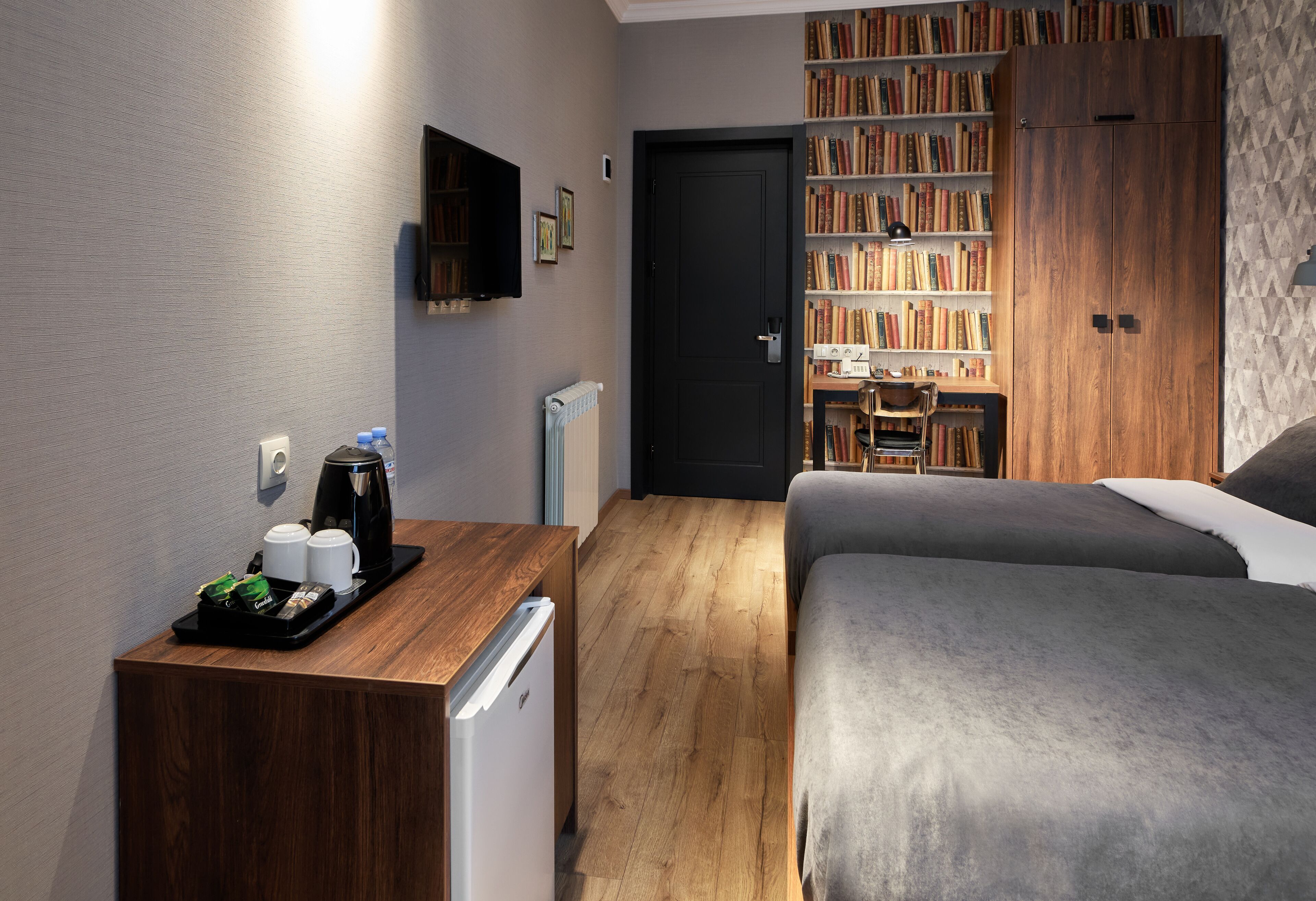 A hotel room with a bed, a desk with a coffee maker, a bookshelf, and a wardrobe.