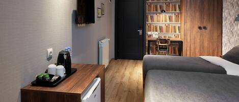 A hotel room with a bed, a desk with a coffee maker, a bookshelf, and a wardrobe.