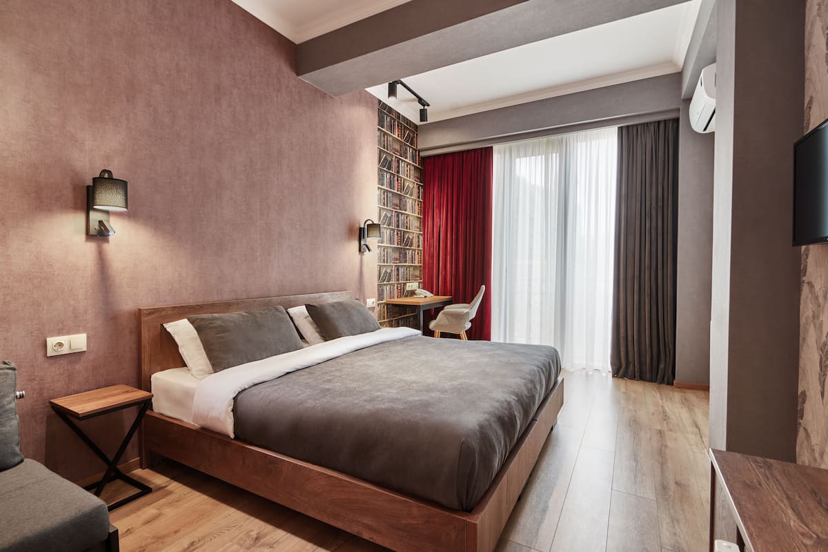 A modern bedroom with a wooden bed, a side table, a bookshelf, and a desk with a chair.
