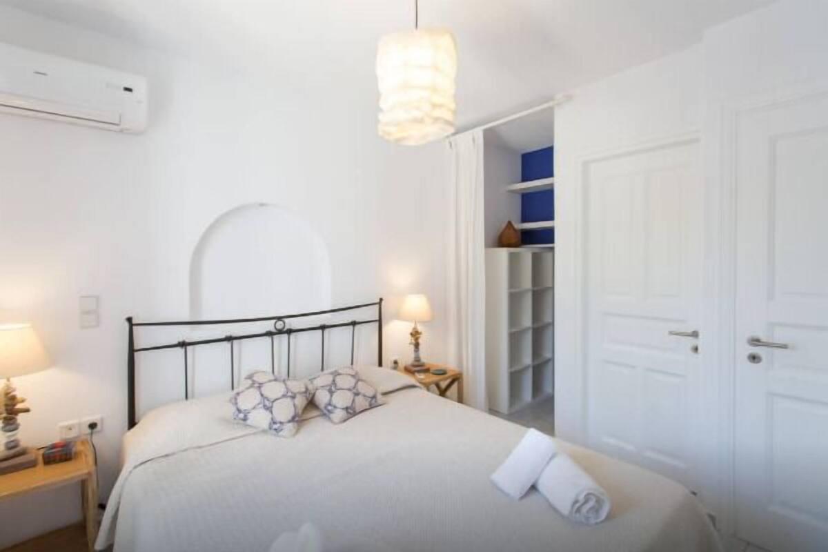 Quarto com cama, mesas de cabeceira, abajur, ar condicionado e guarda-roupa.