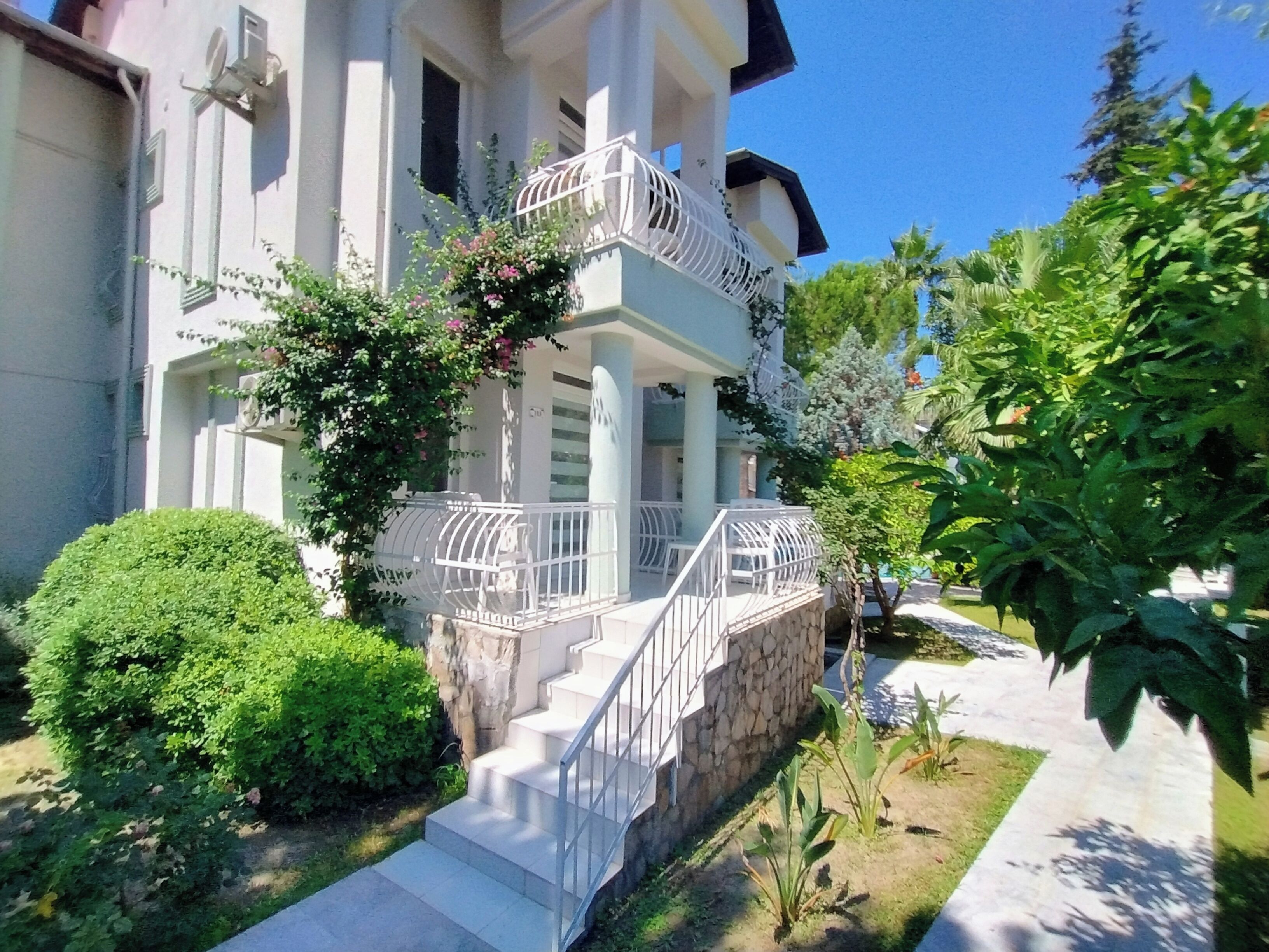 A two-story building with a balcony, a stone wall, and a well-maintained garden.