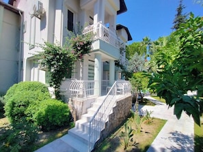 A two-story building with a balcony, a stone wall, and a well-maintained garden. -  Göcek Selya Hotel (Fethiye)