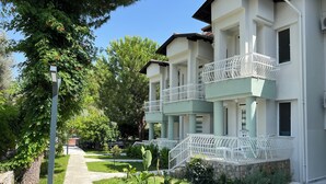 Un edificio a più piani con balconi, un vialetto lastricato e vegetazione circostante.