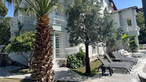 Una casa a due piani con un balcone, una palma e una fila di poltrone da relax.
