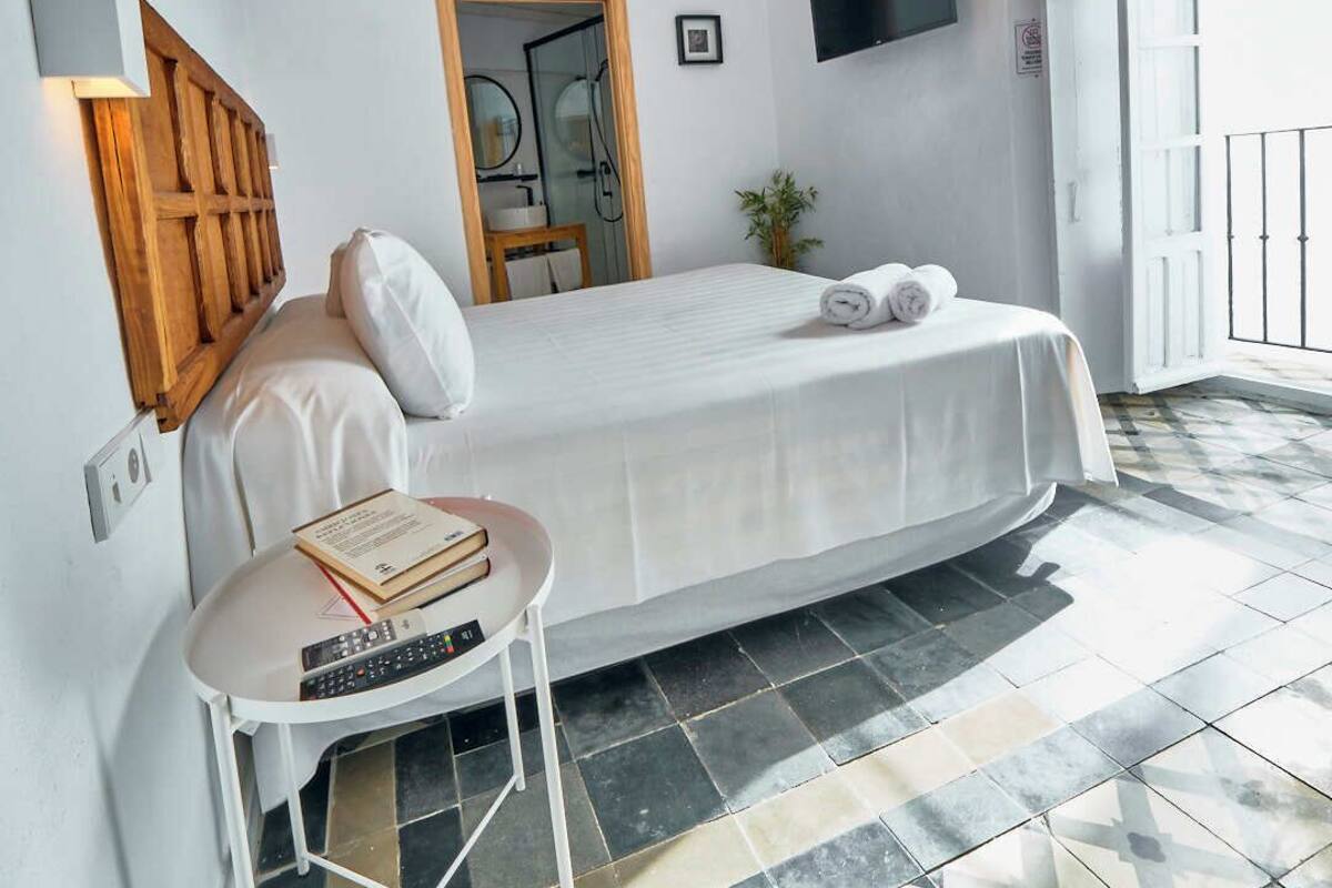 A bedroom with a bed, bedside table, lamp, and a television on the wall.