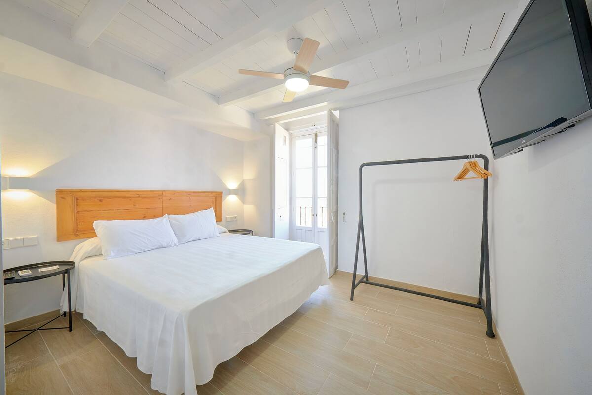 A hotel room with a bed, a TV, a ceiling fan, and a door leading to an outdoor area.