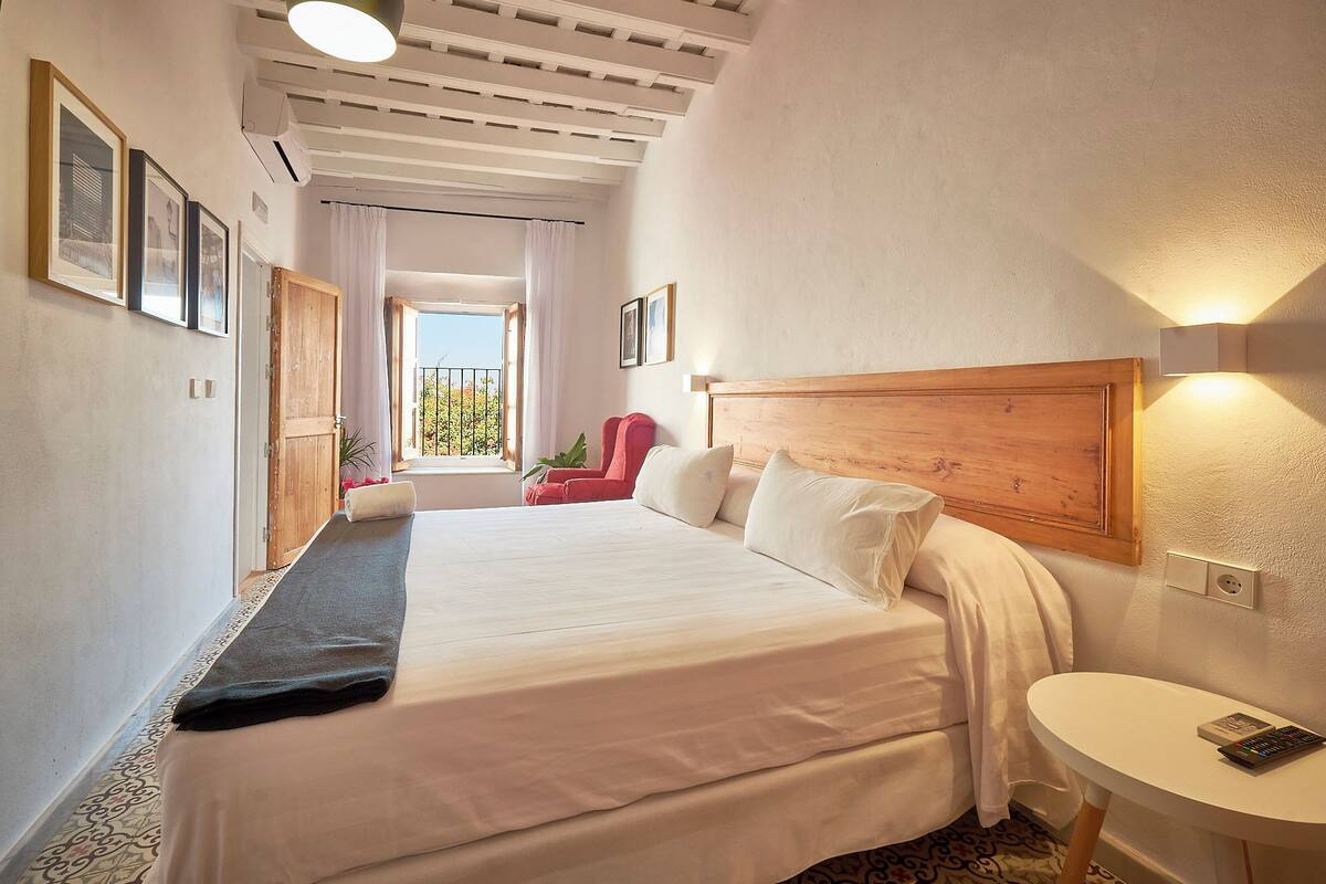 A hotel room with a large bed, a bedside table, a chair, and a window with curtains.