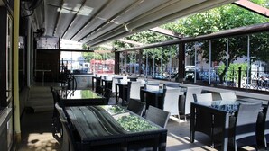 Un patio al aire libre con mobiliario de mimbre, una mesa de vidrio y vistas a la calle.