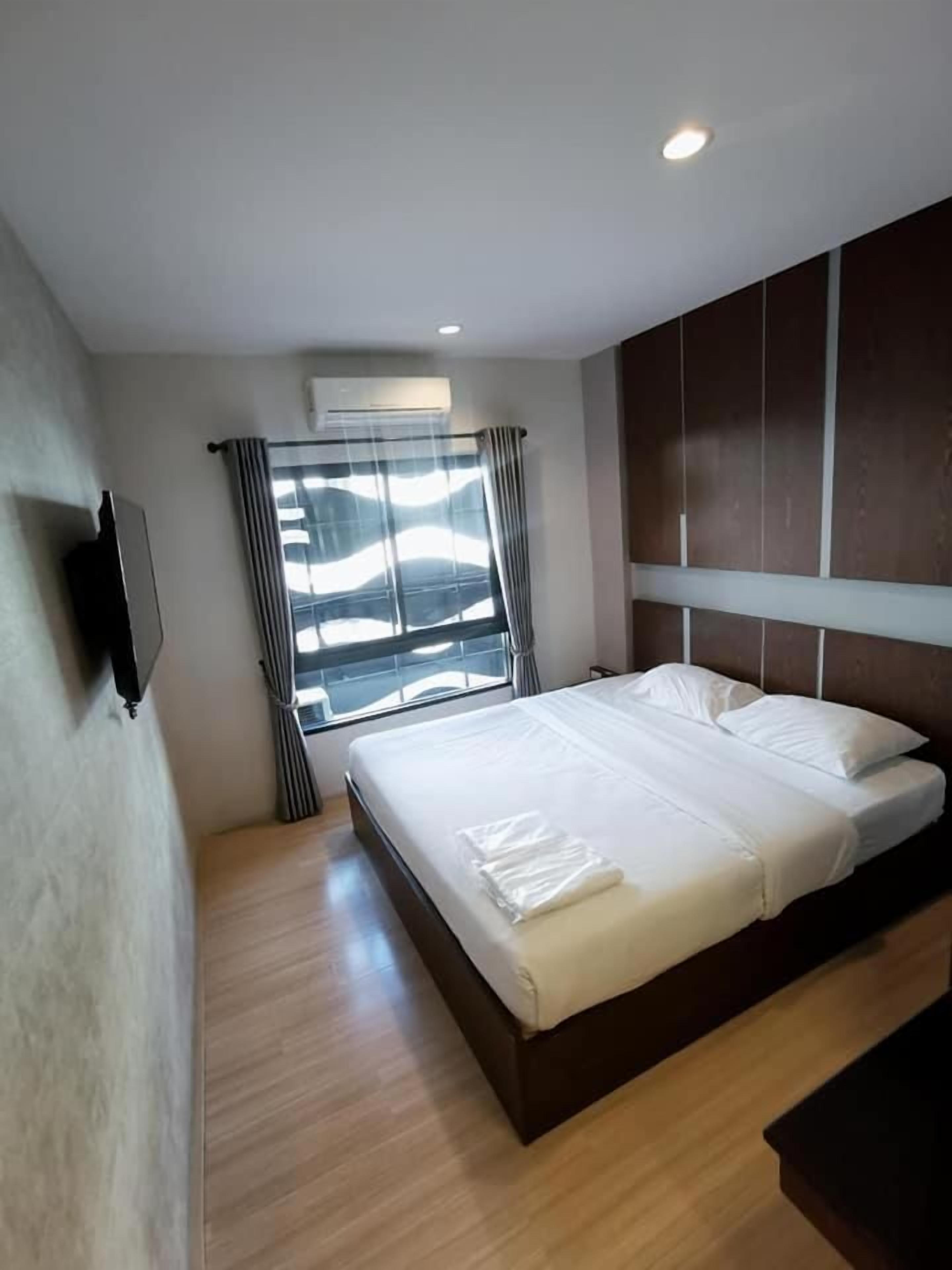 A modern hotel room with a large bed, a flat-screen TV mounted on the wall, and a window with curtains.