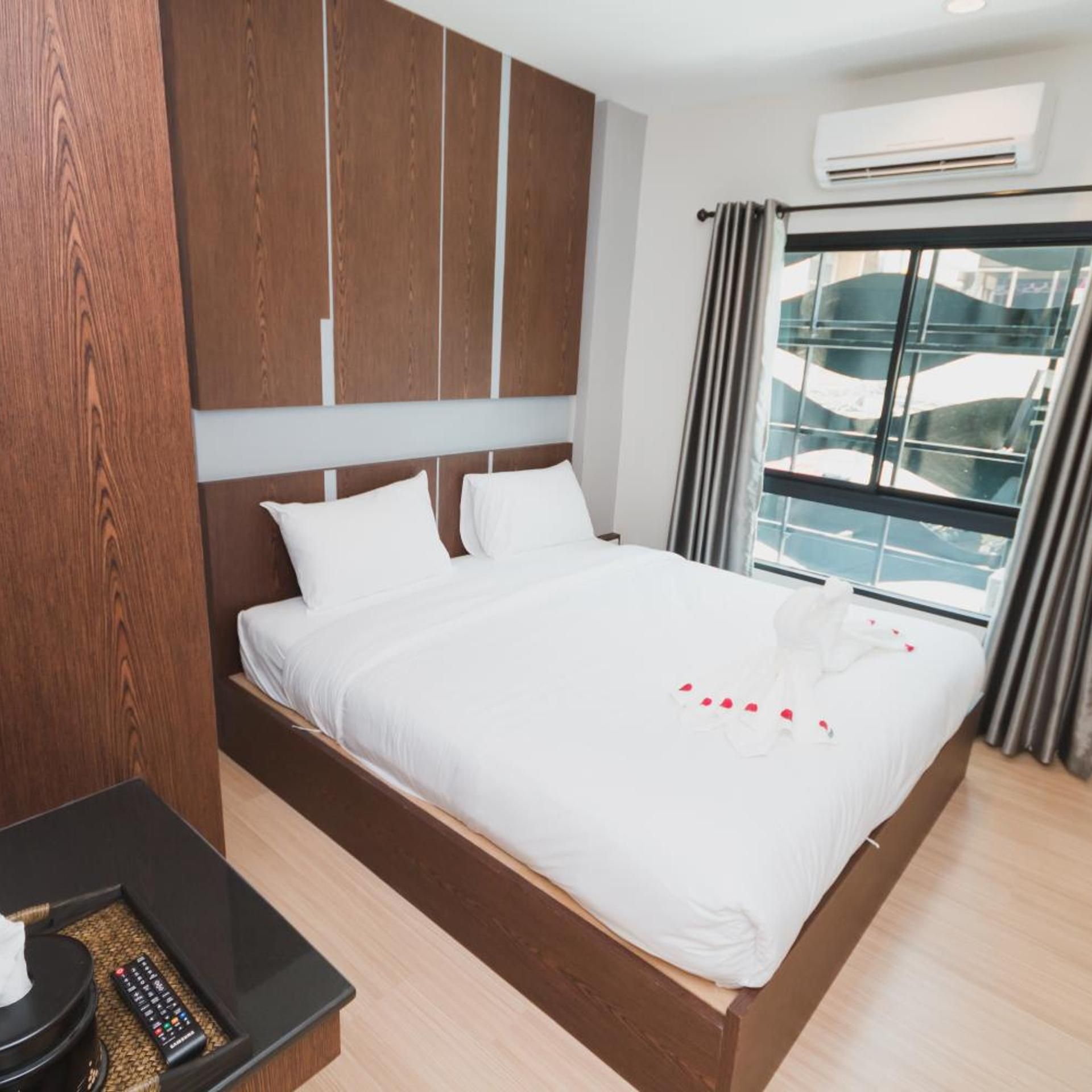 A hotel room with a large bed, wooden headboard, a small bedside table, and a window with a view of buildings.