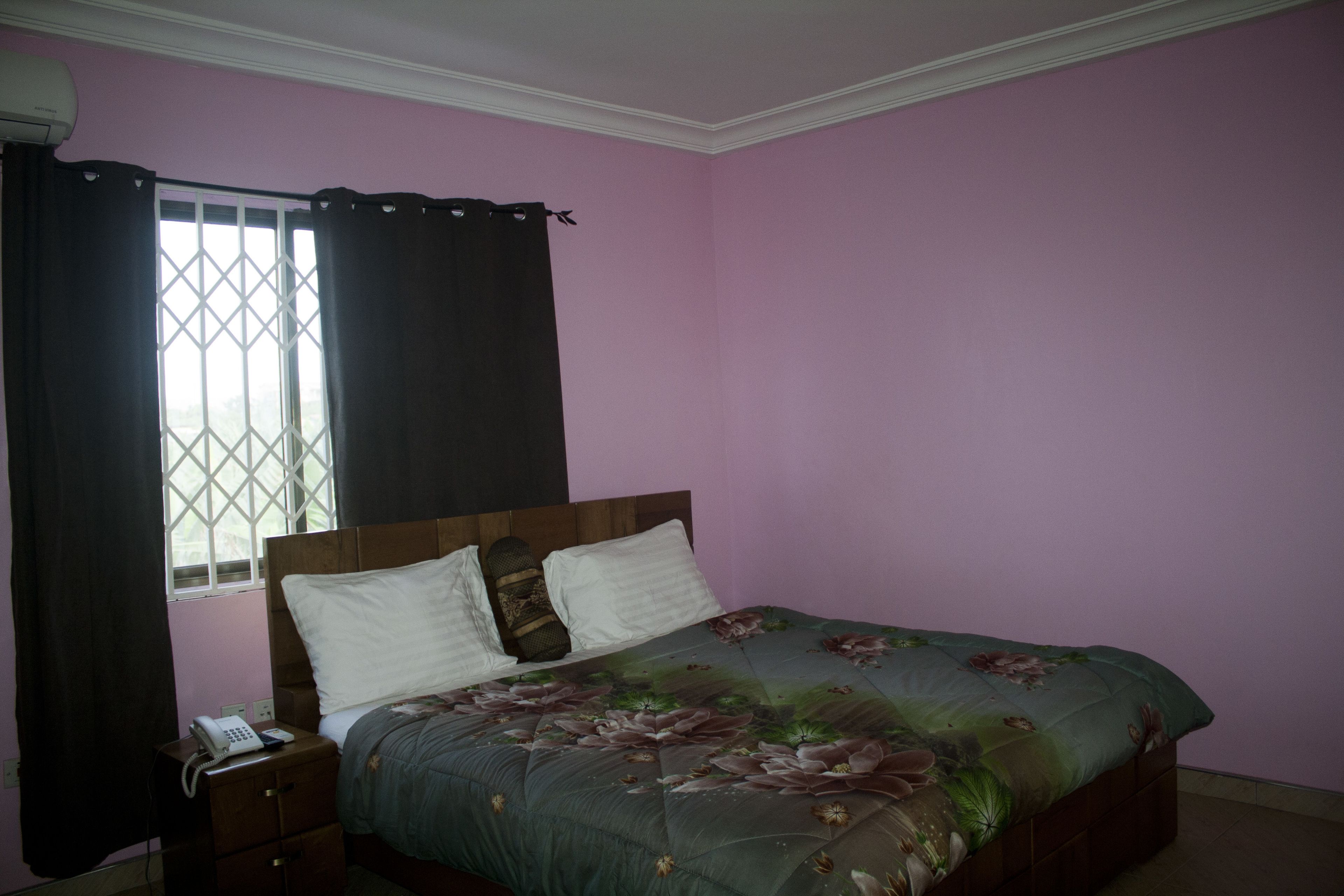 Quarto com cama, mesa de cabeceira, telefone e janela com cortinas.