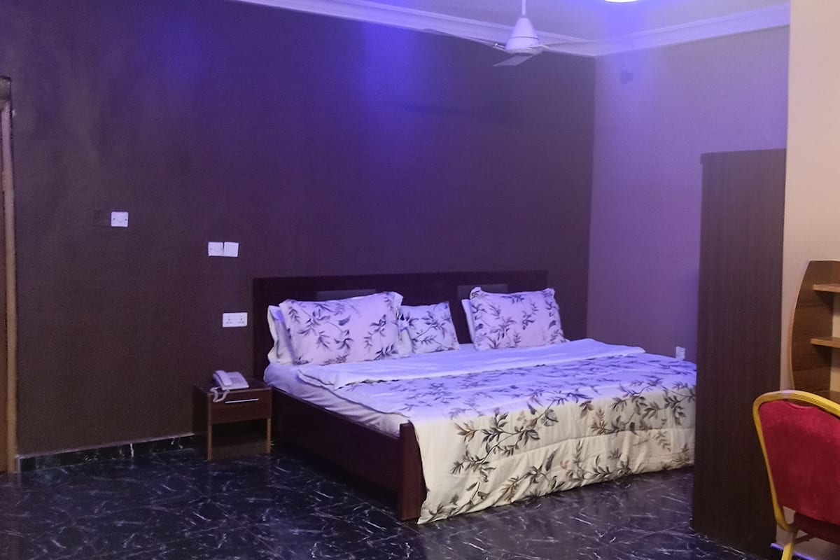 Um quarto com cama, mesa de cabeceira, uma cadeira e um aparador de madeira.