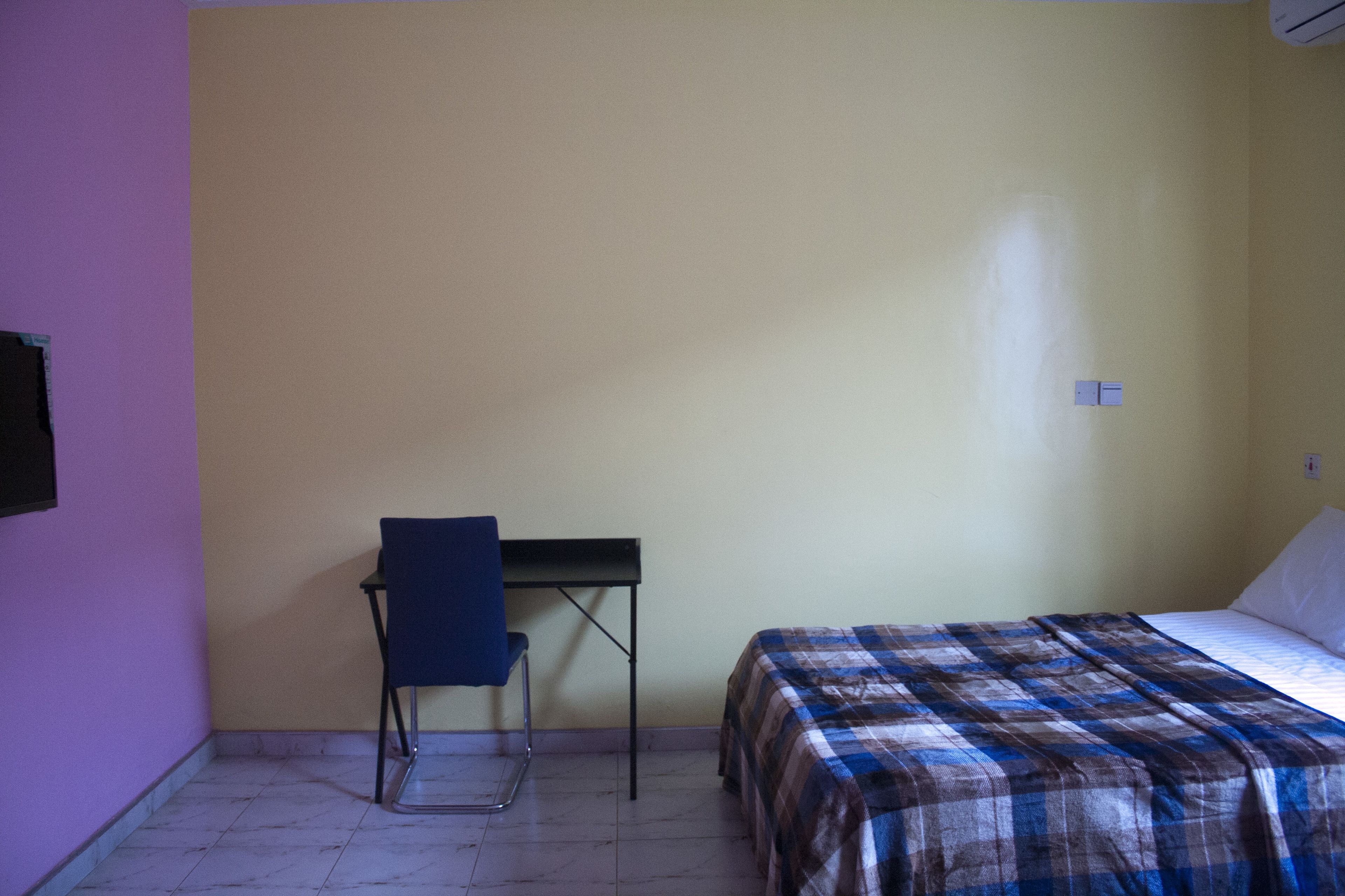 A small, simple room with a bed, a chair, and a desk.