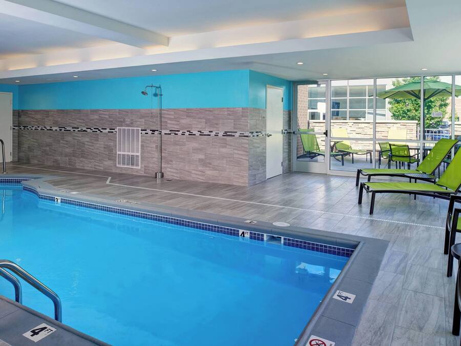 A swimming pool with a tiled edge, a glass door leading outside, and green lounge chairs.