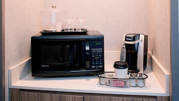A kitchen counter with a microwave, coffee maker, and a basket with a coffee cup and two glasses.