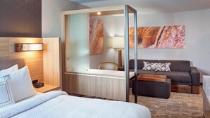 A hotel room with a bed, a desk with a lamp, a sofa, and a large mirror. - Springhill Suites Grand Rapids West (Grandville)