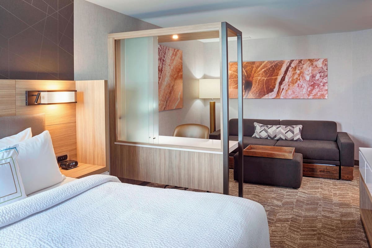 A hotel room with a bed, a desk with a lamp, a sofa, and a large mirror.