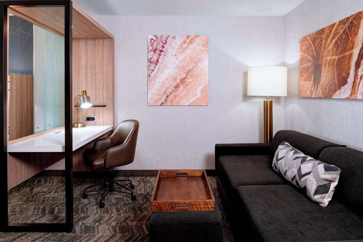 A hotel room with a desk, chair, sofa, and a small wooden tray table.