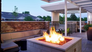 An outdoor patio with a fire feature, seating, and a covered area. - Springhill Suites Grand Rapids West (Grandville)