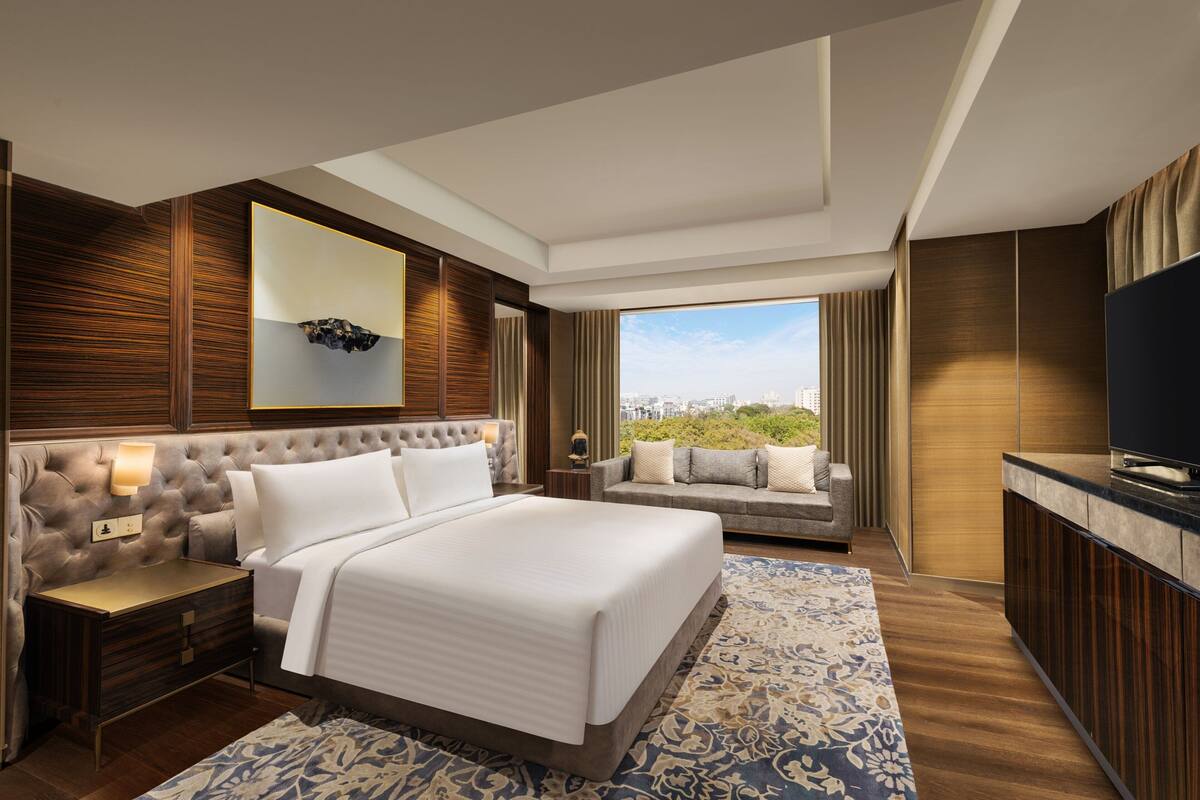 A modern hotel room with a large bed, a TV, a desk, and a view of the city.