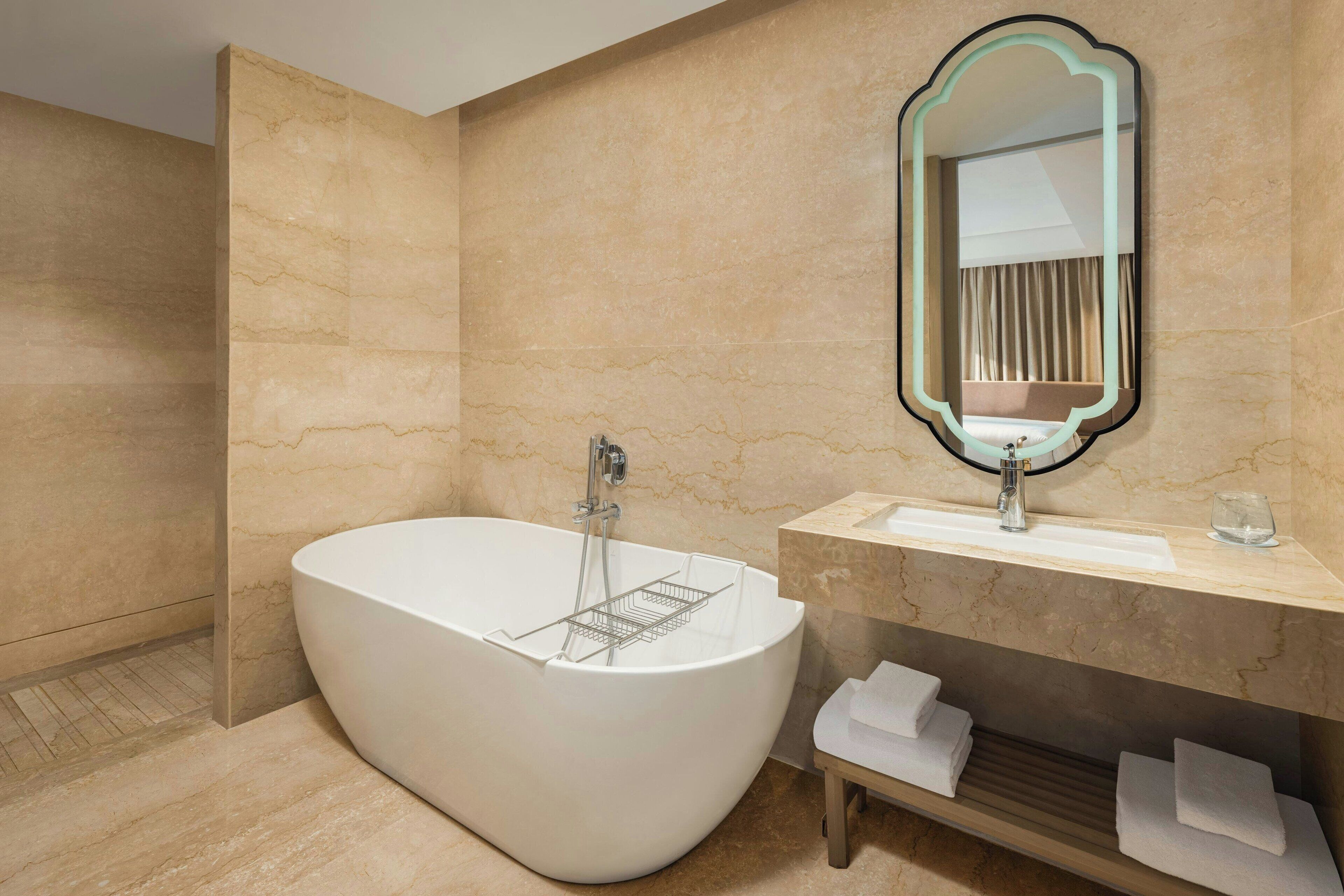 A modern bathroom with a freestanding bathtub, a marble wall, a vanity with a mirror, and a towel rack.