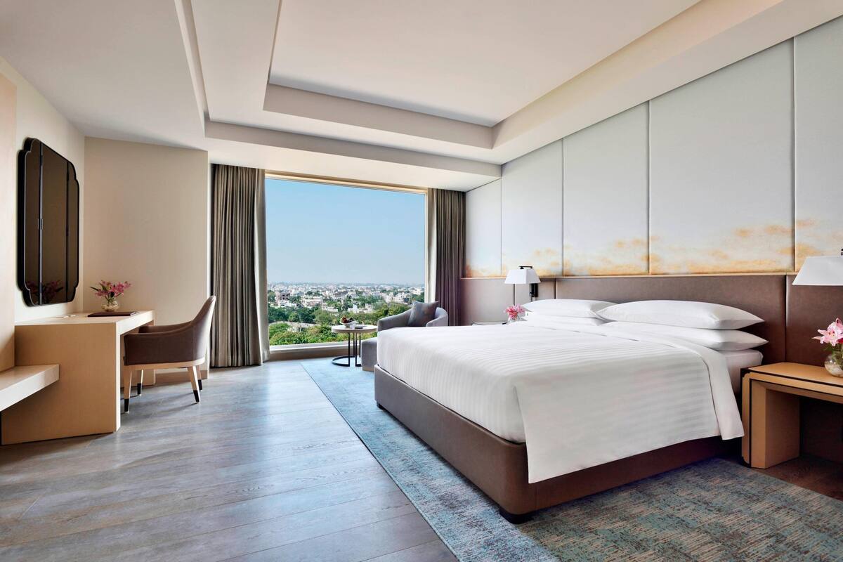 A modern hotel room with a large bed, a desk, a chair, and a view of the city.