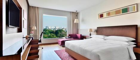 A modern hotel room with a large bed, a TV, a desk, and a view of the city.