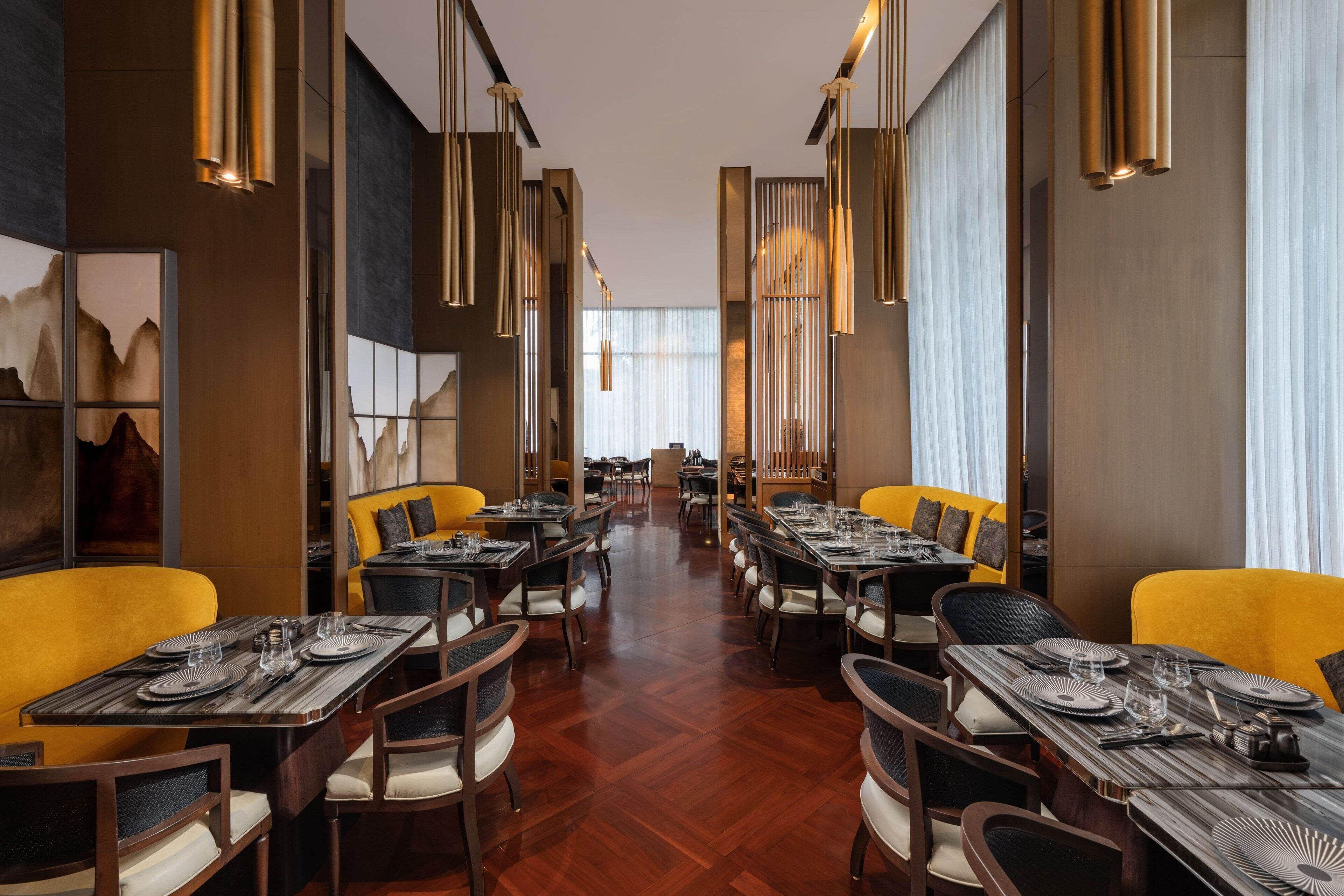 A restaurant with multiple dining tables and chairs, arranged in a spacious layout with high ceilings and modern pendant lighting.