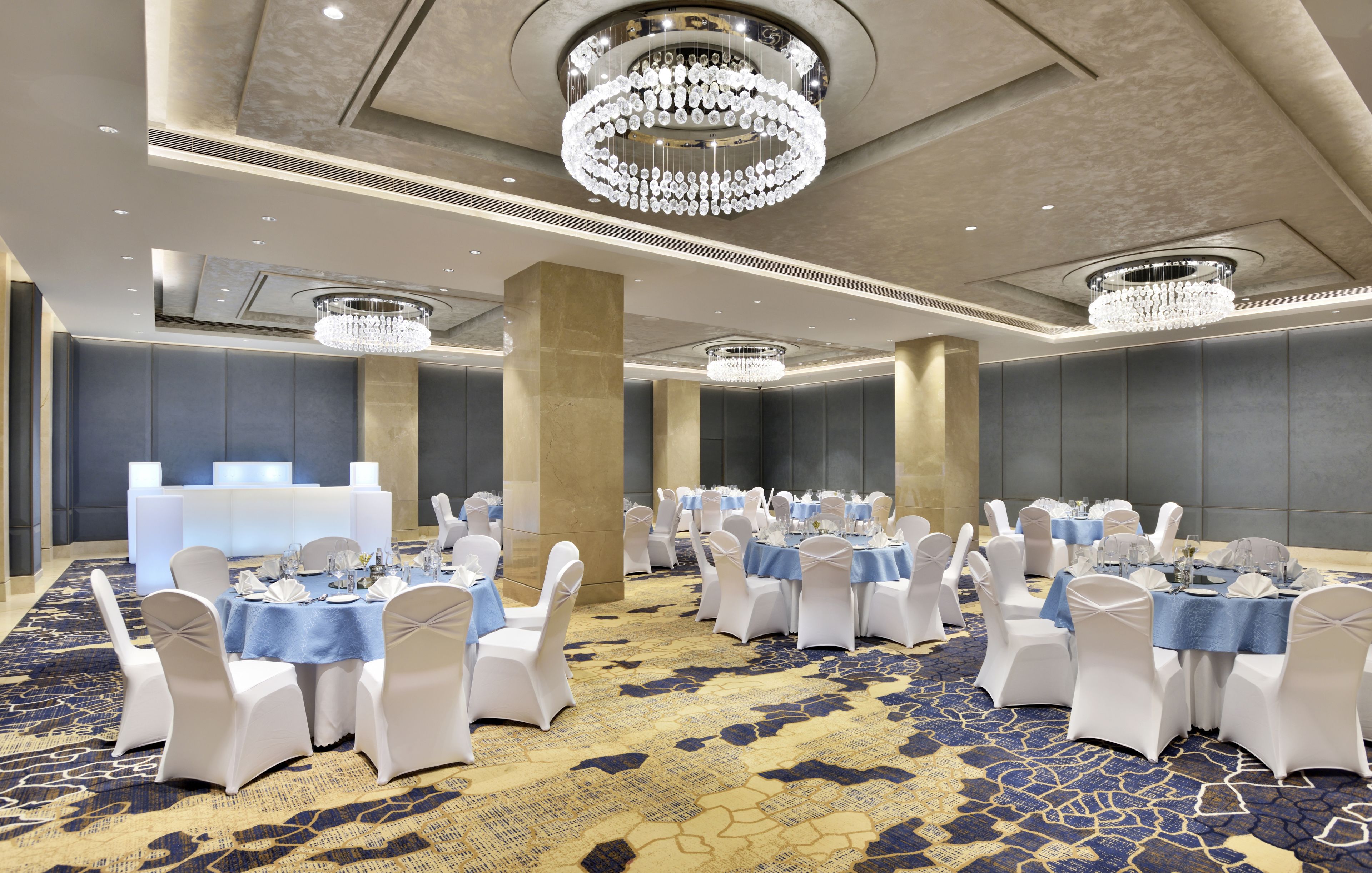 A banquet hall with round tables, white chairs, and chandeliers.
