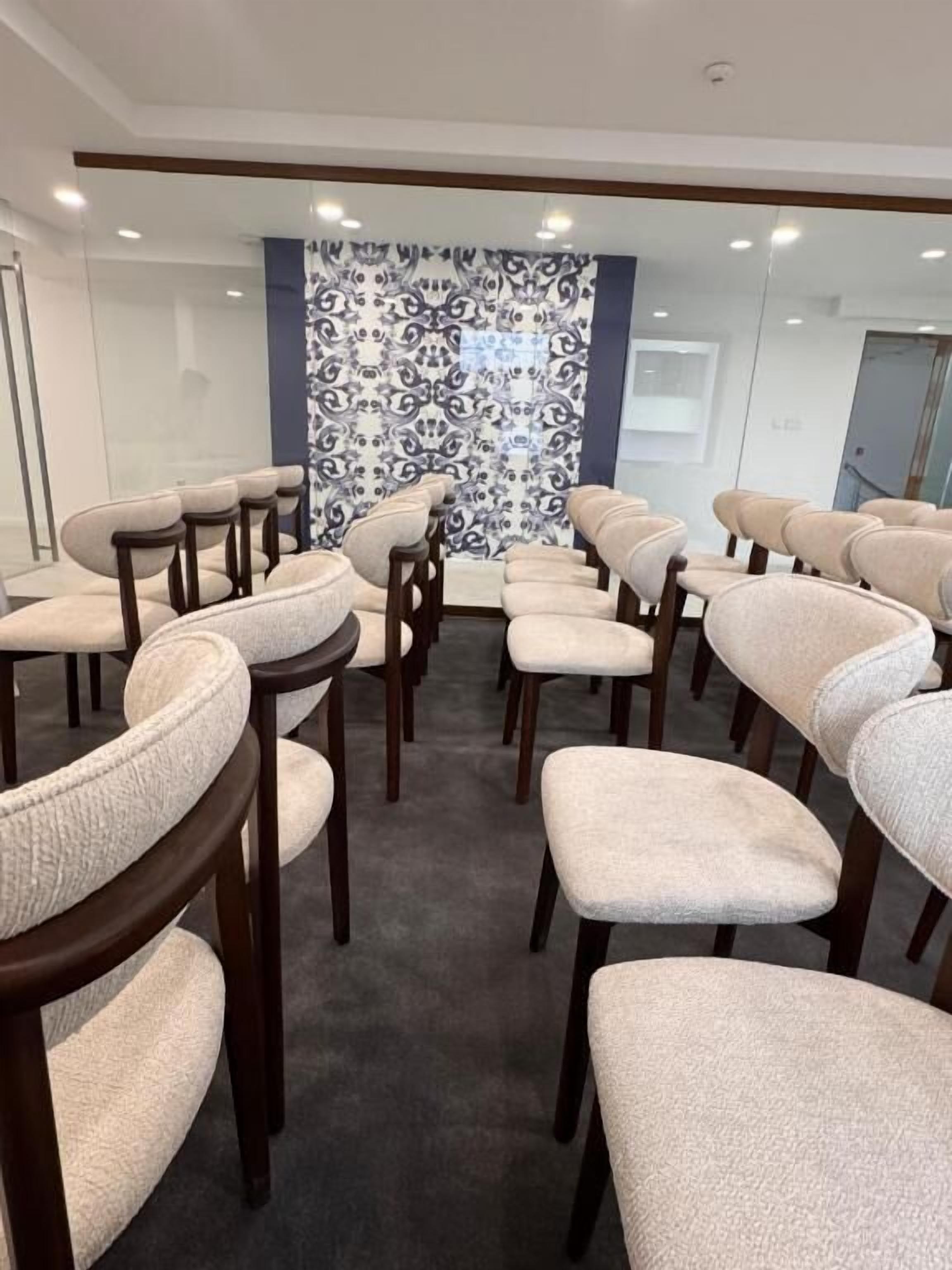 A conference room with rows of chairs, a patterned wall, and a glass partition.