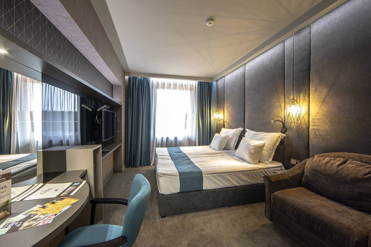 A hotel room with a bed, a desk, a chair, and a sofa.