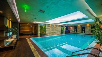 A modern indoor swimming pool with a skylight, wooden flooring, and potted plants.