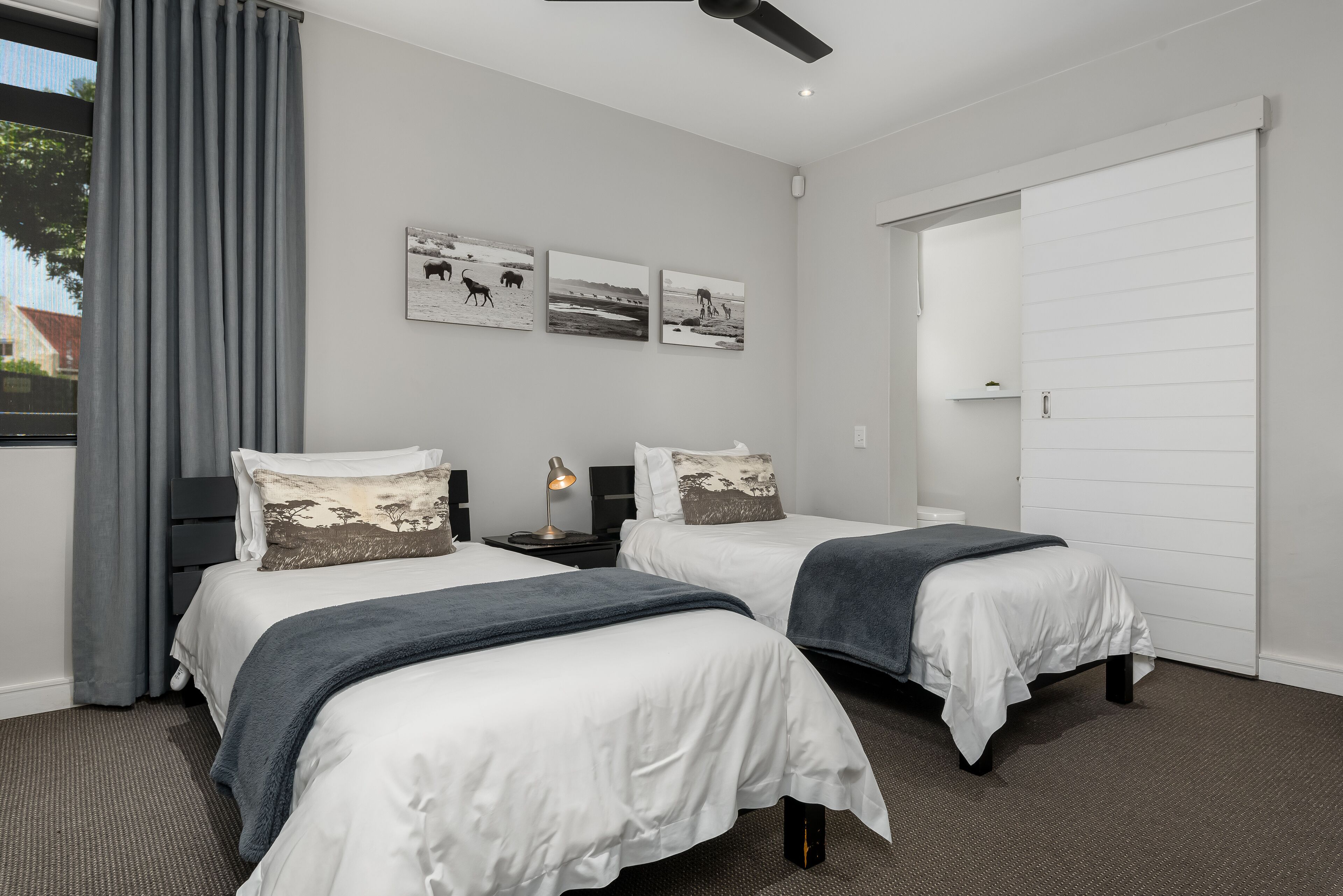 A modern hotel room with two beds, a ceiling fan, and artwork on the wall.