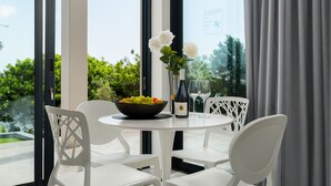 A round table with white chairs, a bowl of fruit, a wine bottle, and a vase with white flowers. - Sunset Splendour Guesthouse (Cape Town)