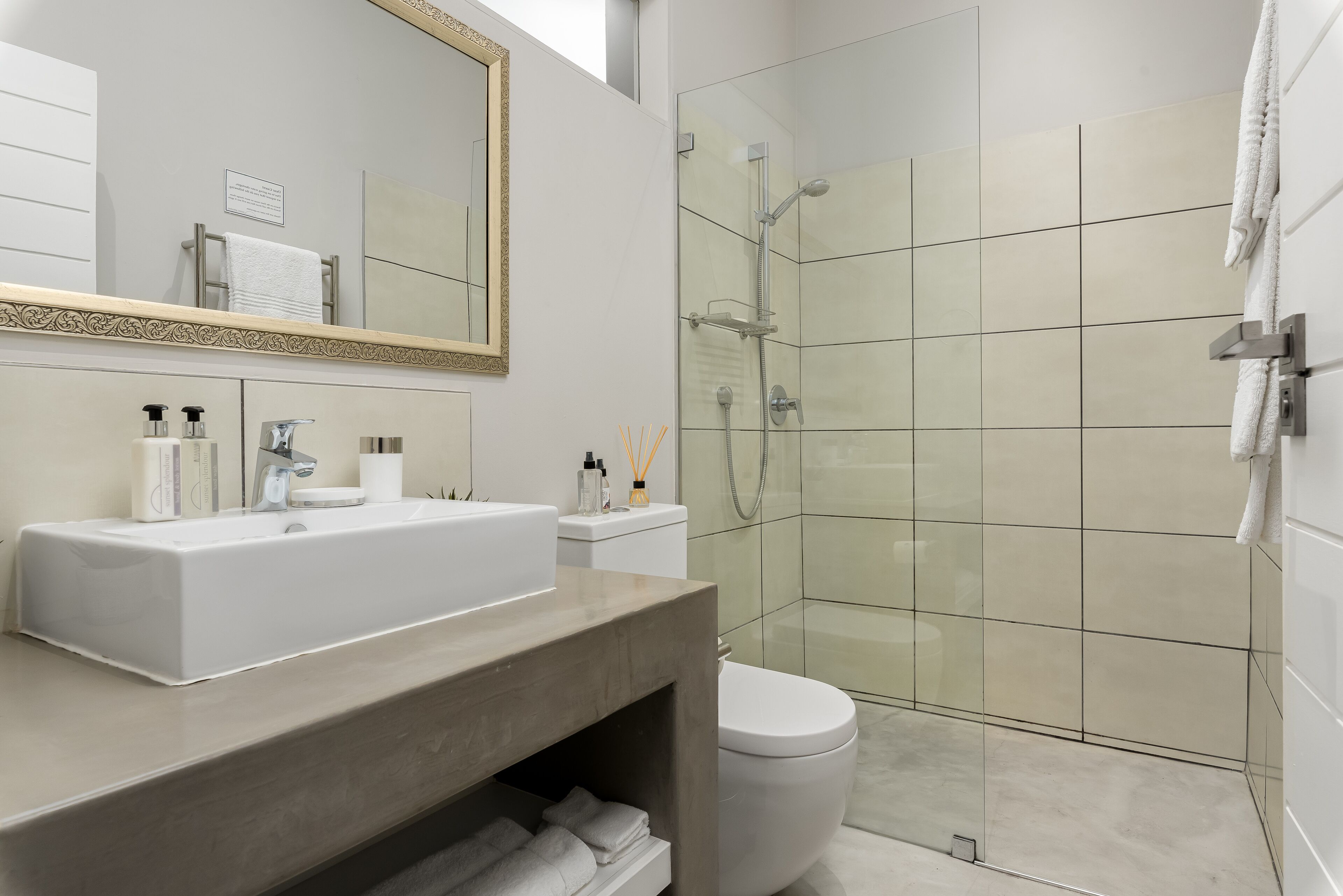 A modern bathroom with a large mirror, a sink, a toilet, and a glass-enclosed shower.