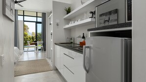 A modern kitchen with white cabinets, a black countertop, and a built-in refrigerator. There is a window with a view of greenery outside. - Sunset Splendour Guesthouse (Cape Town)